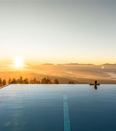 Una piscina moderna con vista sulle montagne all'alba. I raggi d'oro del sole si riflettono sull'acqua.