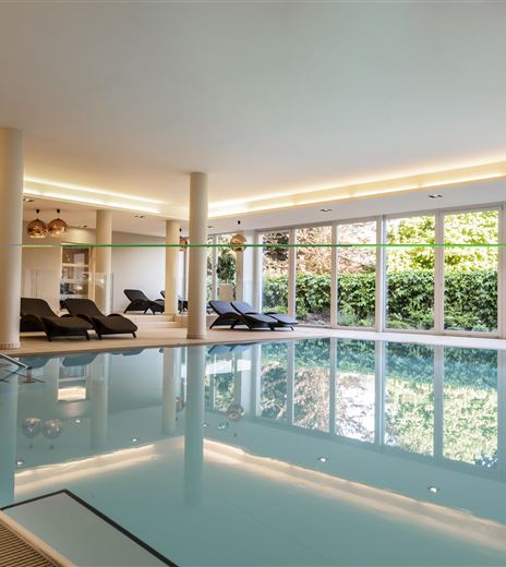 Una elegante piscina interna con illuminazione moderna e ampie finestre. Letti comodi invitano a fermarsi.