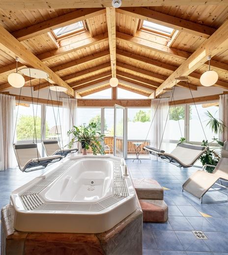 Un accogliente centro benessere con una vasca idromassaggio e lettini moderni. Grandi finestre lasciano entrare molta luce diurna e creano un'atmosfera rilassante.