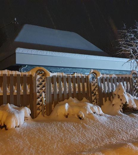 Ein Haus im Schnee bei Nacht. Der Garten ist mit einer dicken Schneeschicht bedeckt und der Zaun ist teilweise eingeschneit.