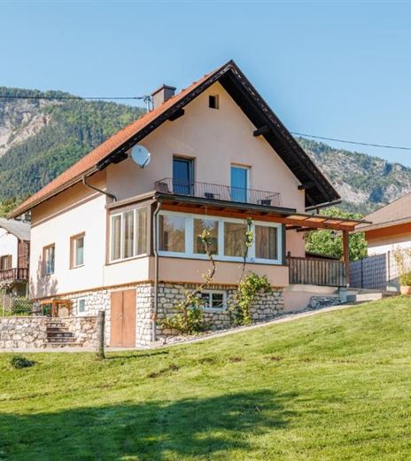 Una bellissima casa bifamiliare con un giardino curato e vista sulle montagne. La facciata è luminosa e offre grandi finestre e una veranda.