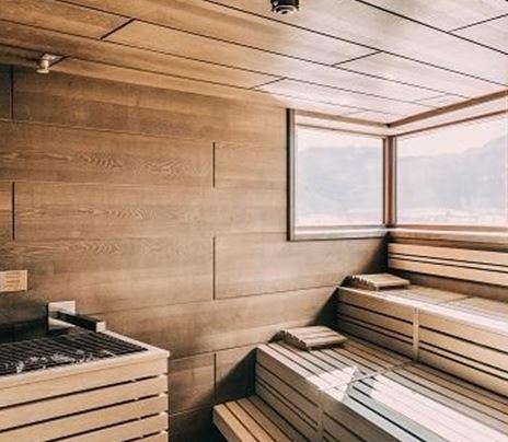 Una sauna moderna con rilievi in legno e grandi finestre. La stanza è luminosa e accogliente.