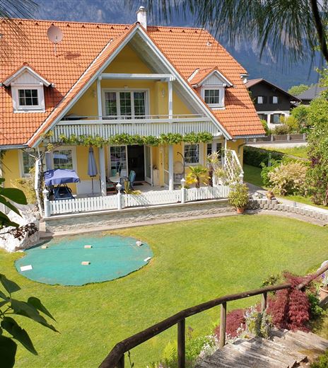 Una bellissima casa con un tetto rosso e una grande veranda.  
Il giardino è verde e accogliente, con un piccolo prato e piante colorate.
