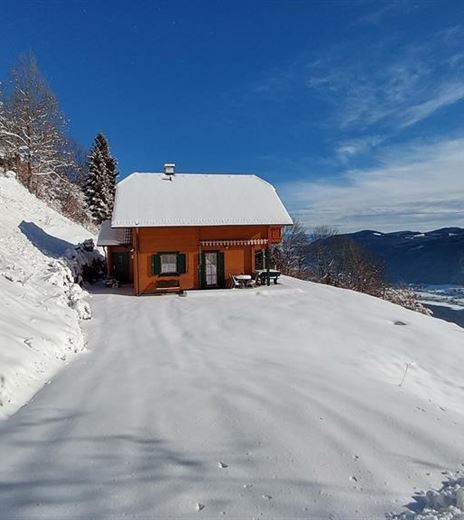 Una casa accogliente di colore arancione in un paesaggio innevato. Gli alberi circostanti sono coperti di neve, e il cielo è sereno e blu.
