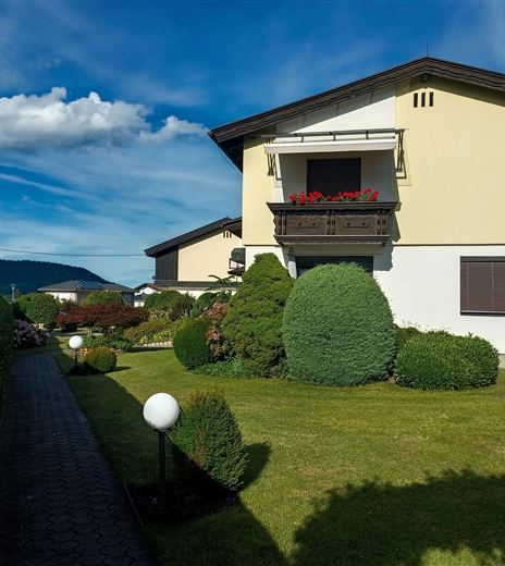 Una bella casa con un giardino e un breve sentiero. Il sole di mezzogiorno splende su un ombrellone giallo.