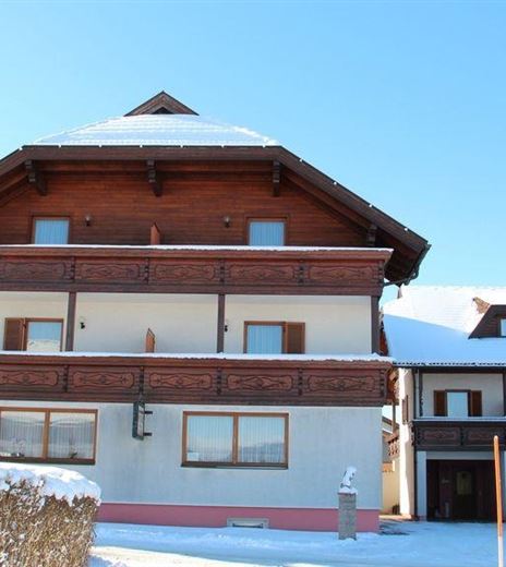 A beautiful building in winter with a snow-covered roof and clear blue sky. Surrounding the house is snow and a hedge.