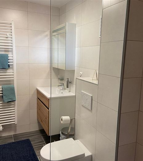 Un bagno moderno con piastrelle bianche e un lavabo in legno. Asciugamani e una doccia sono anch'essi presenti.