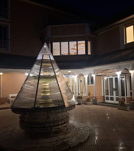 Ein moderner Innenhof mit einem dreieckigen Glasobjekt und beleuchteten Eingängen. Die Atmosphäre ist gemütlich und einladend, besonders bei Nacht.