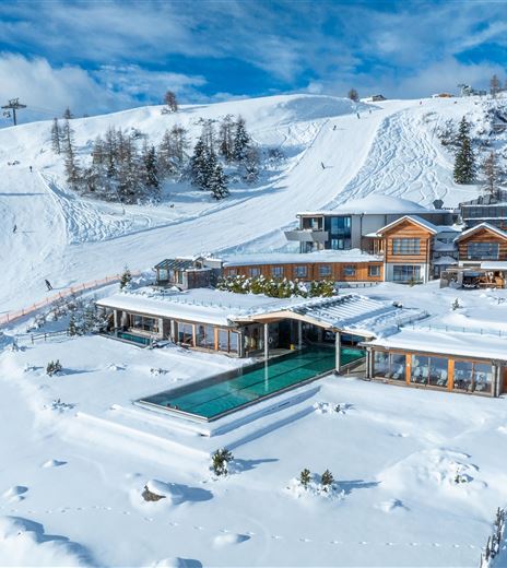 Un moderno chalet immerso in un paesaggio coperto di neve. In primo piano è visibile una piscina, circondata da montagne innevate.