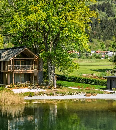 Ein schönes modernes Holzhaus am Ufer eines ruhigen Sees. Umgeben von grünen Bäumen und einer malerischen Landschaft.