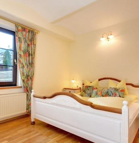 Ein gemütliches Schlafzimmer mit einem großen Bett und bunten Vorhängen. Die Holzfußböden verleihen dem Raum eine warme Atmosphäre.