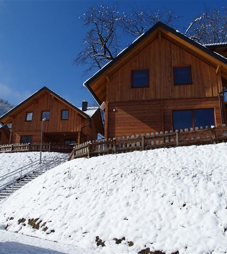Tre case vacanze rivestite in legno si trovano su un versante coperto di neve. Il cielo blu limpido e il paesaggio invernale circostante creano un'atmosfera meravigliosa.