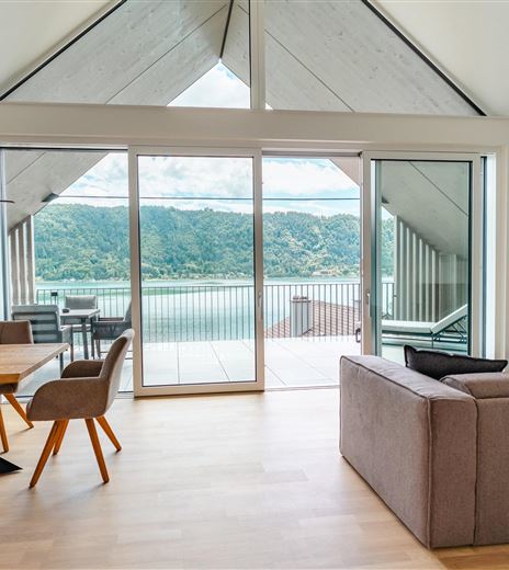 Ein modernes Wohnzimmer mit großen Fenstern und Blick auf eine grüne Landschaft. Der Raum ist hell und gemütlich mit einer klaren, offenen Gestaltung.