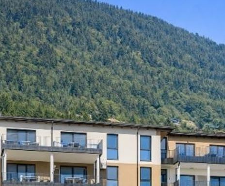Un moderno edificio residenziale ai piedi di una collina boschiva. Il cielo blu e limpido completa la piacevole vista.