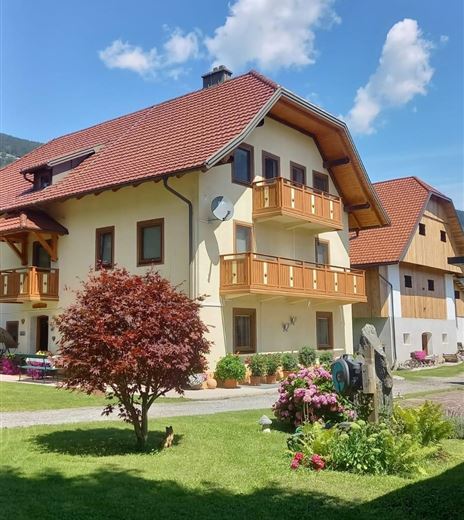 Ein hübsches Gebäude mit einem roten Dach und Balkonen. Es gibt einen gepflegten Garten mit Blumen und einem kleinen Baum.