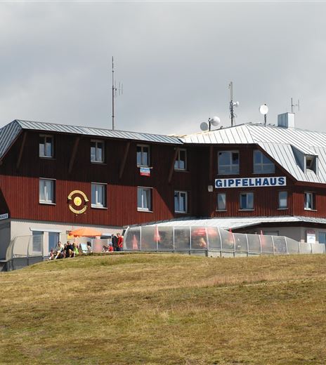 Ein rotes Gebäude mit einem grauen Dach steht auf einem Hügel. Es ist das "Stippelhaus" und umgeben von grünen Wiesen.
