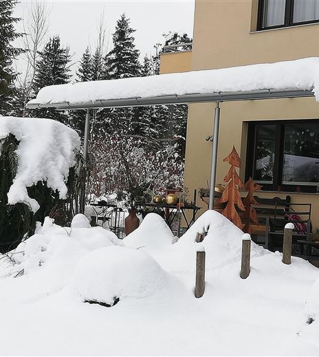 Ein verschneiter Garten vor einem Haus. Schnee bedeckt die Bäume und den Boden.