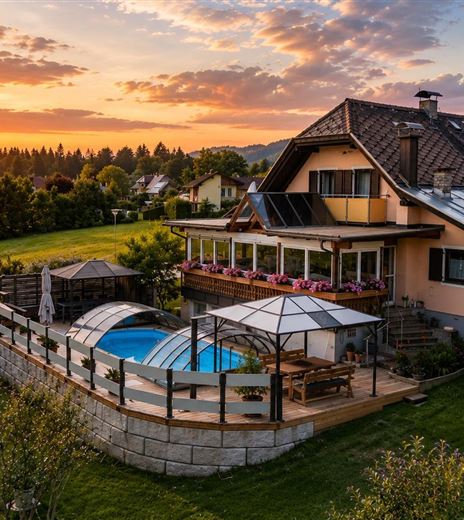 Ein schönes Haus mit einem Pool und einer Terrasse, umgeben von grünen Wiesen. Im Hintergrund erleuchtet der Sonnenuntergang den Himmel.