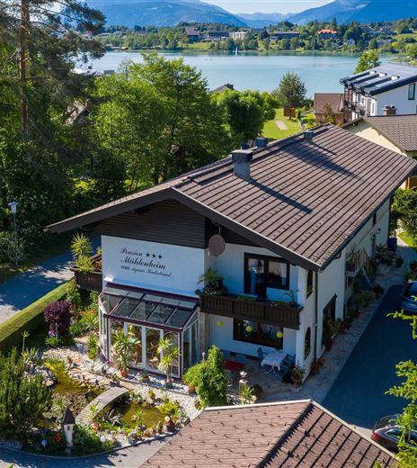 Una casa per ospiti incantevole con un giardino curato vicino a un lago. Sullo sfondo si vedono montagne e un paesaggio pittoresco.