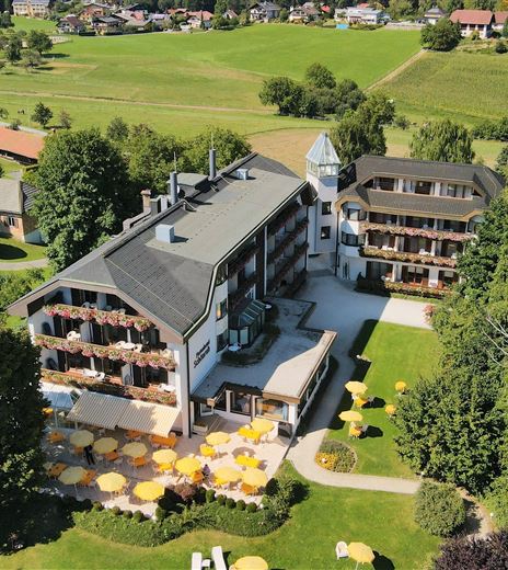 Un edificio alberghiero pittoresco circondato da prati e alberi verdi. Ombrelloni gialli invitano a rilassarsi all'aperto.