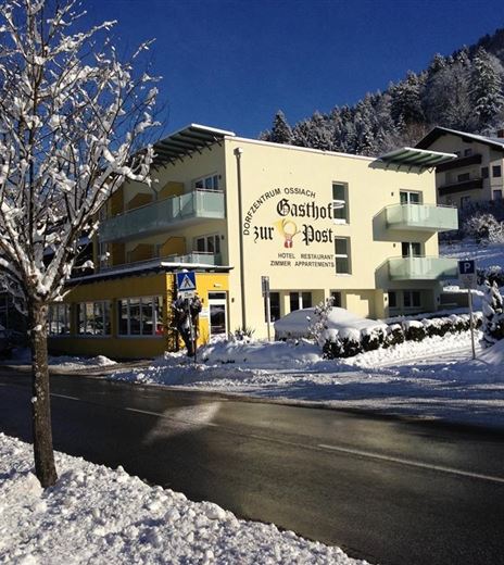 An inn called "Zur Post" in a snowy landscape. Surrounded by trees and a clear sky, the surroundings are wintry and inviting.