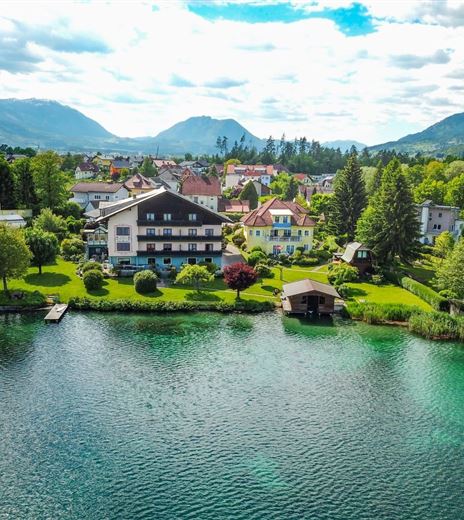 Una vista pittoresca di un lago, circondato da prati verdi e alberi. Sullo sfondo si vedono dolci colline e una città affascinante.