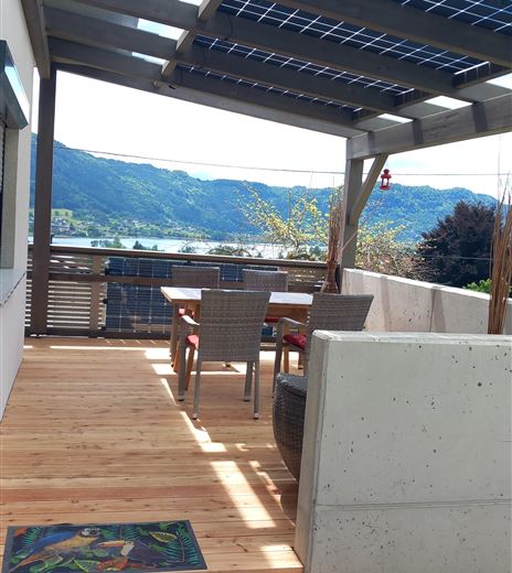 Eine moderne Terrasse mit Holzfußboden und einem Essbereich. Im Hintergrund sind Hügel und ein klarer Himmel sichtbar.