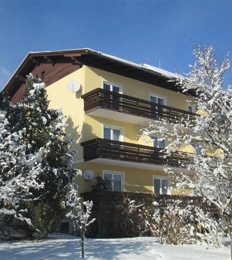 Un edificio giallo nella neve con molti alberi e rami innevati. Il cielo è blu e sereno.