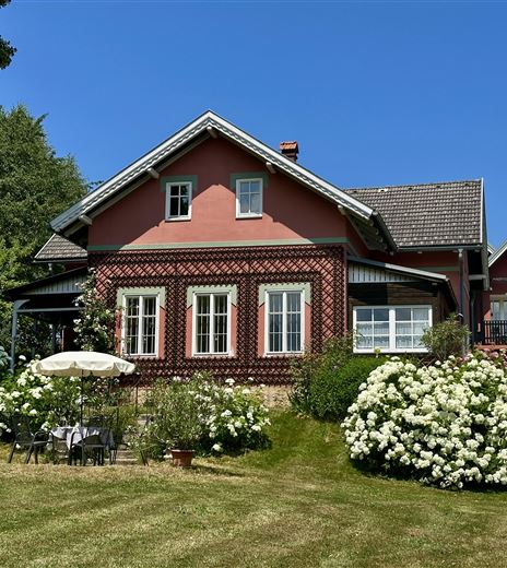 Ein charmantes Haus mit roter Fassade und weißen Fenstern. Der Garten ist üppig bewachsen mit blühenden Sträuchern und lädt zum Entspannen ein.