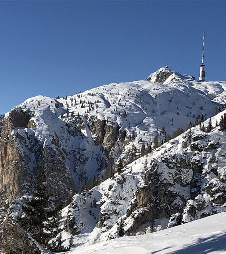 Una montagna coperta di neve con un traliccio sulla cima. Il cielo blu chiaro offre un bel contrasto con il paesaggio invernale.
