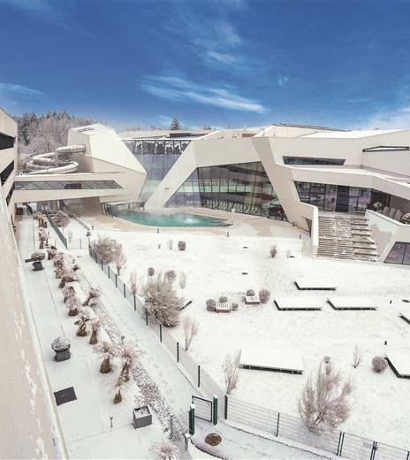 Eine moderne Architektur im Winter, umgeben von Schnee. Der Himmel ist klar und blau, und die Anlage ist elegant gestaltet.