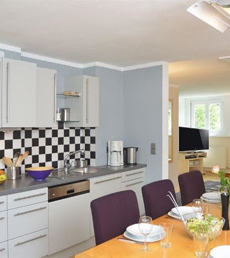 Eine moderne Küche mit einem schwarz-weißen Fliesenmuster und einem Esstisch. Der Raum ist hell und einladend, mit einem Wohnzimmer im Hintergrund.