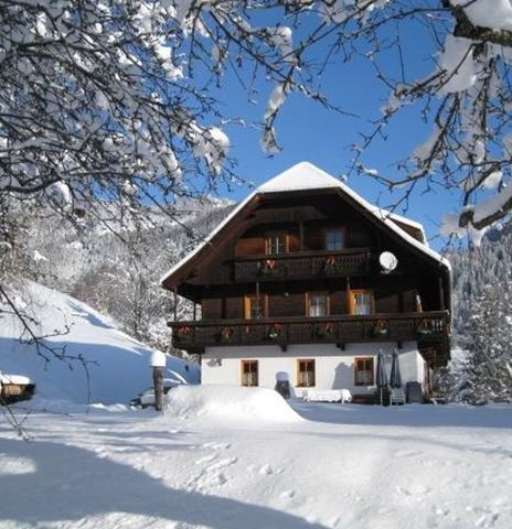 Ein schönes, schneebedecktes Alpenhaus umgeben von Winterlandschaft. Der klare blaue Himmel kontrastiert mit dem weißen Schnee.