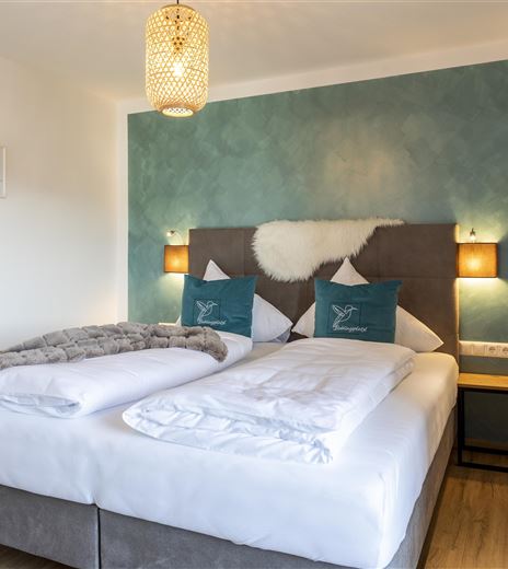 Una camera da letto moderna con un grande letto matrimoniale e biancheria da letto accogliente. Le pareti sono dipinte di un blu delicato, arricchite da lampade eleganti e decorazioni.