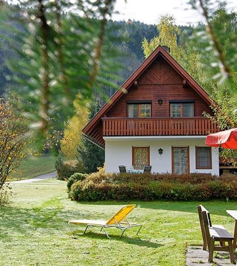 Ein gemütliches Ferienhaus umgeben von grüner Natur. Im Vordergrund stehen Gartenmöbel und ein Sonnenschirm.
