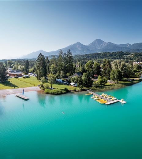 Un lago tranquillo con acqua limpida e turchese e aree costiere verdi. Sullo sfondo si vedono montagne imponenti e un bel paesaggio.