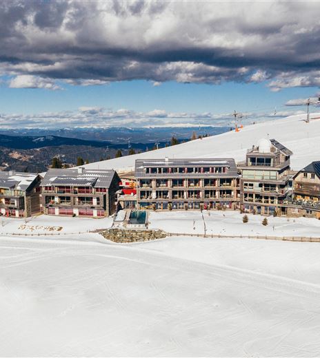 Un paesaggio montano pittoresco innevato con diversi edifici moderni. Il cielo è parzialmente nuvoloso e offre una vista impressionante.
