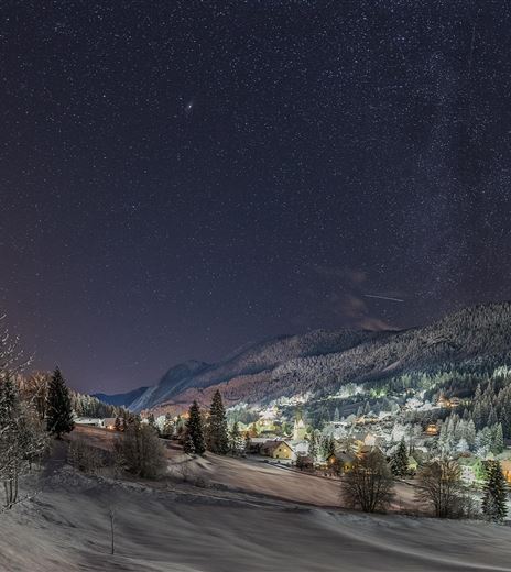 Un paesaggio invernale pittoresco con colline coperte di neve e un piccolo villaggio sotto un cielo stellato. L'ambiente è tranquillo e pacifico, perfetto per una notte invernale.