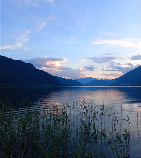 A tranquil lake surrounded by mountains and gentle hills. The sky is painted in soft shades of blue and pink.