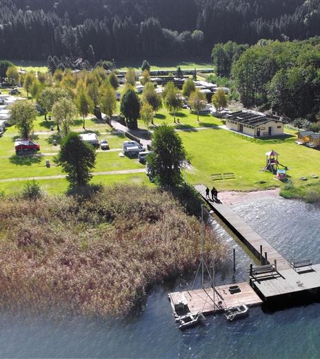 Un bel campeggio vicino all'acqua con un pontile. Circondato da alberi e verde rigoglioso.
