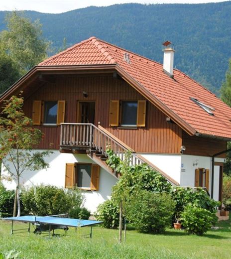 Una casa accogliente con un tetto in tegole rosse e rivestimento in legno.
Il giardino è verde e invitante, circondato da alberi e piante.