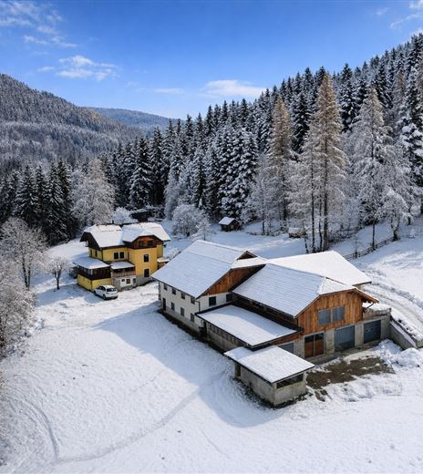 Eine winterliche Landschaft mit schneebedeckten Häusern und frostigen Bäumen. Der Himmel ist blau und die Berge im Hintergrund sind sichtbar.