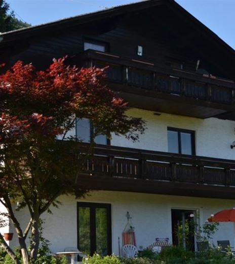 Una bella casa con un balcone e un acero rosso sul davanti. L'ambiente è verde e montuoso.