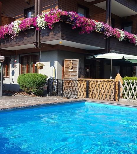 Ein schöner Swimmingpool vor einem Haus mit Blumenbalkonen. Es gibt Liegestühle und Sonnenschirme zum Entspannen.