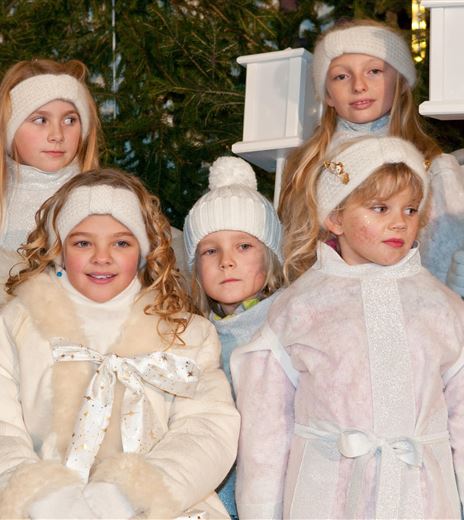 Eine Gruppe von Kindern in winterlichen, festlichen Kleidern steht zusammen. Einige halten Laternen und tragen warme Mützen.