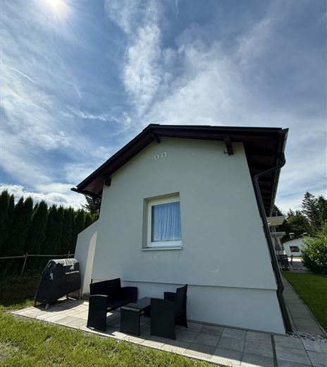 Ein modernes Haus mit einem kleinen Sitzbereich aus schwarzen Möbeln. Der Himmel ist klar und die Umgebung ist grün.