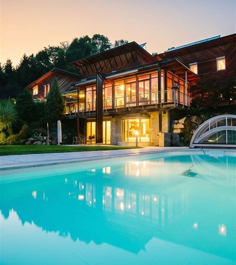 Ein elegantes Haus mit großen Fenstern steht am Rand eines Pools. Die Abenddämmerung sorgt für eine entspannte Atmosphäre.