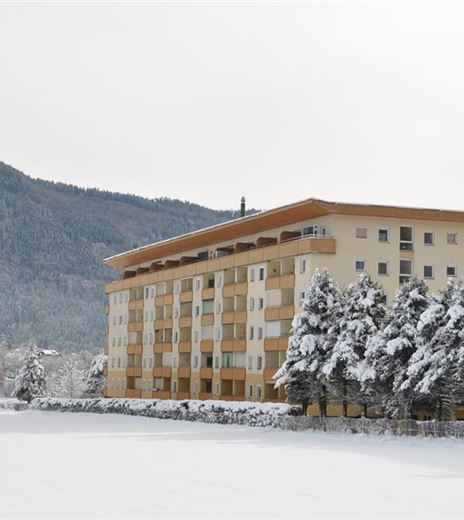 Ein modernes Gebäude in einer verschneiten Landschaft. Im Hintergrund sind schneebedeckte Berge zu sehen.