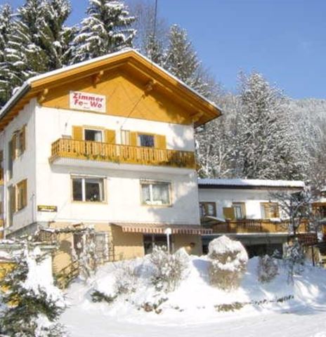 Una accogliente casa vacanze in inverno, circondata da alberi coperti di neve. Il sole splende e il cielo è sereno.