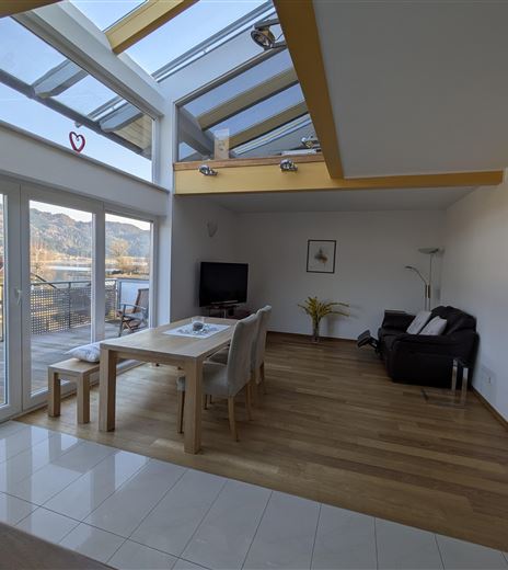 Un soggiorno spazioso con grandi finestre e molta luce naturale. Ci sono un tavolo da pranzo e un'accogliente zona soggiorno con vista sul paesaggio.